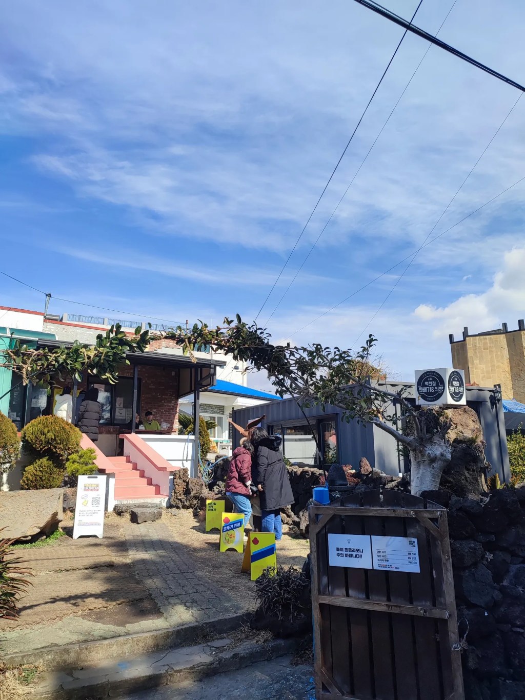 제주도 골목 안에 위치한 백한철꽈배기 매장의 전경, 입구 앞에 손님들이 줄을 서 있는 모습