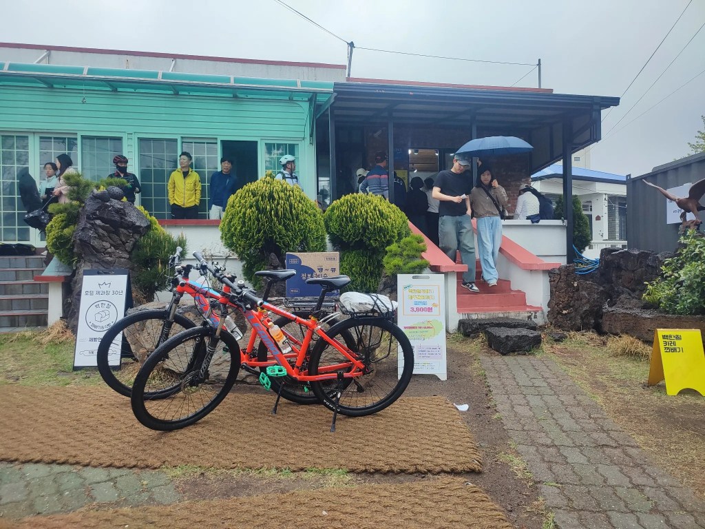 비 오는 날 백한철꽈배기 매장 앞에서 사람들이 줄을 서서 기다리는 모습